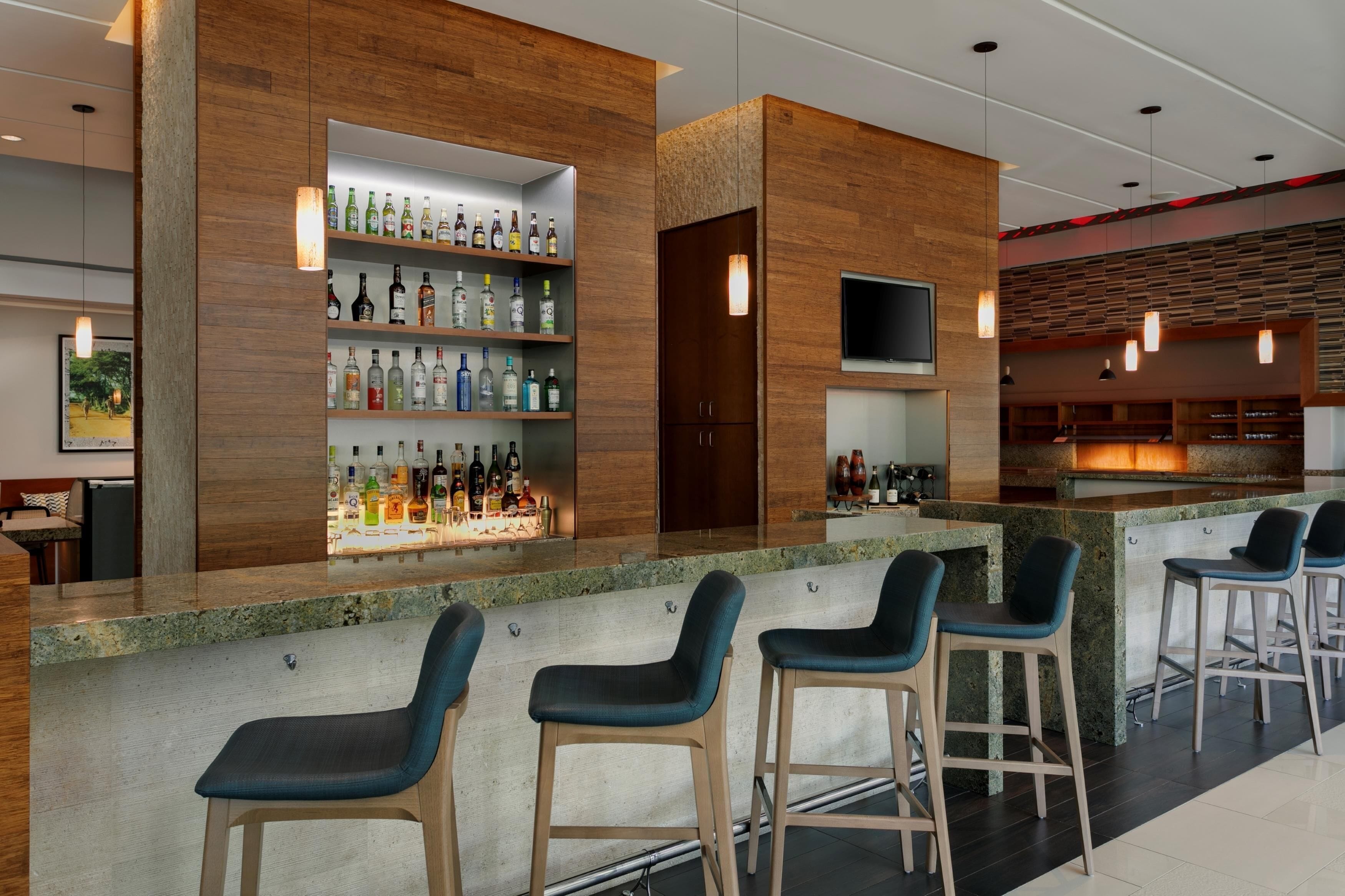 A modern bar area with wooden accents, a variety of liquor bottles, and bar stools.