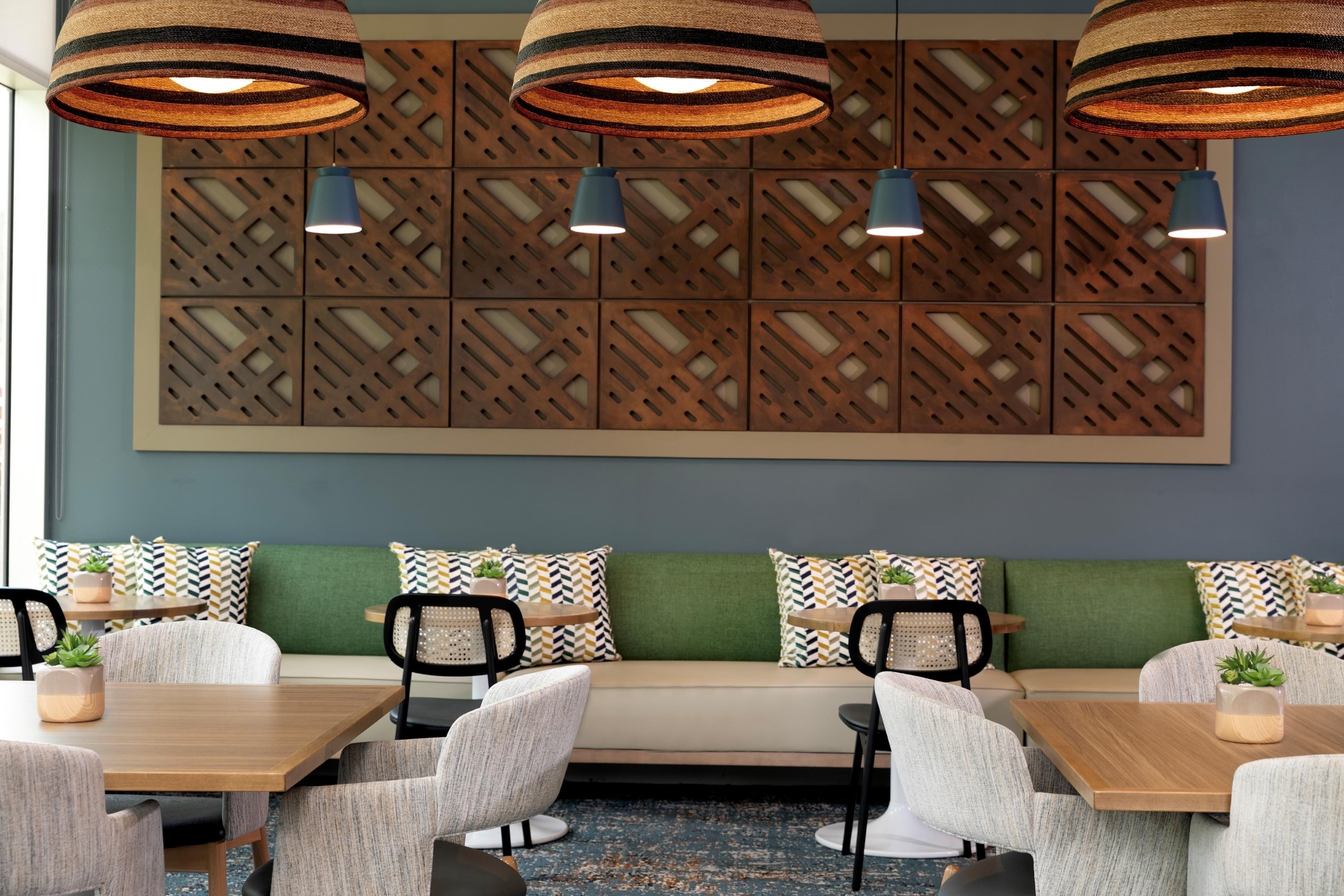 A modern dining area with a long wooden table, cushioned seating, and pendant lighting.