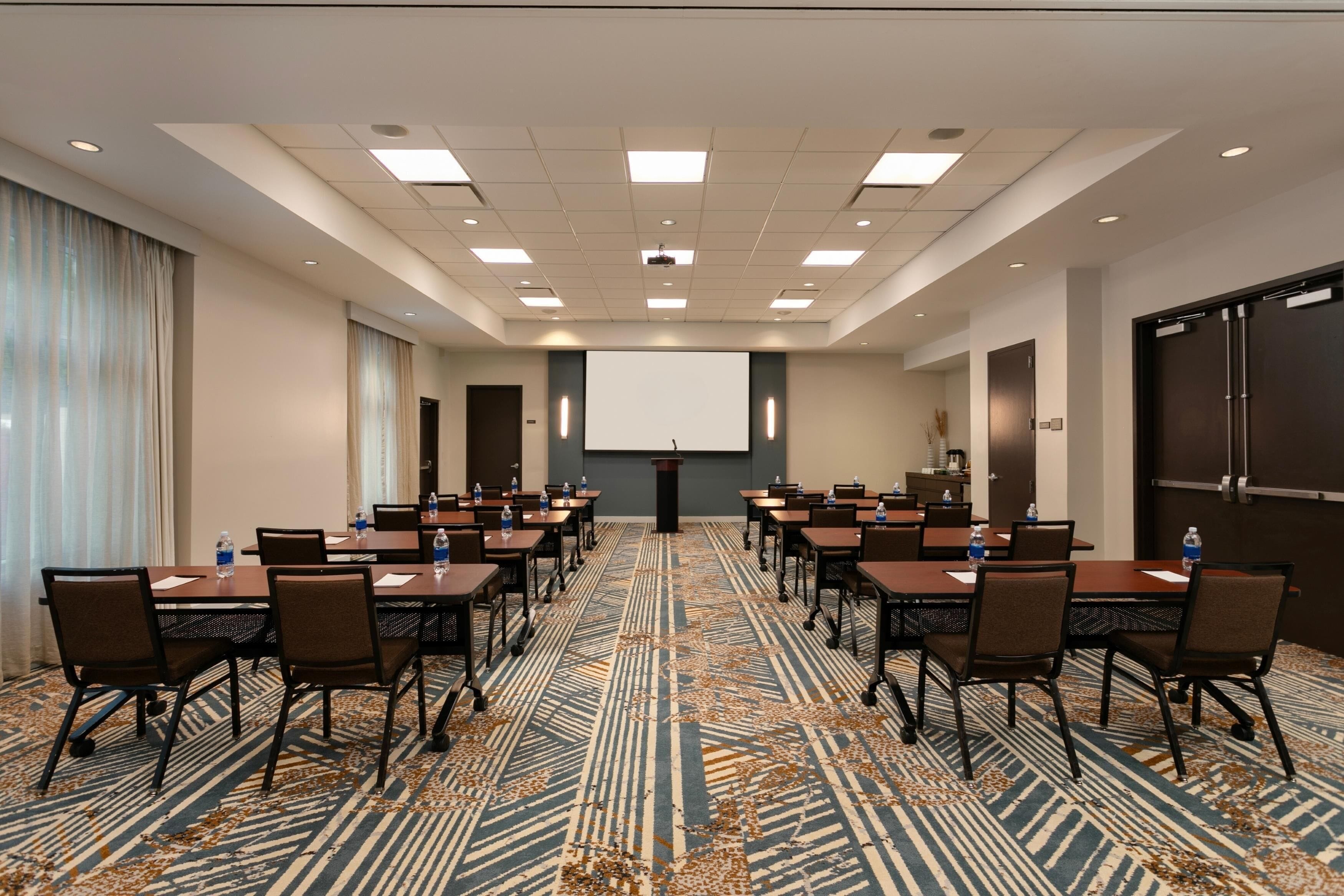 A conference room with a long table, chairs, a projector screen, and a carpeted floor.