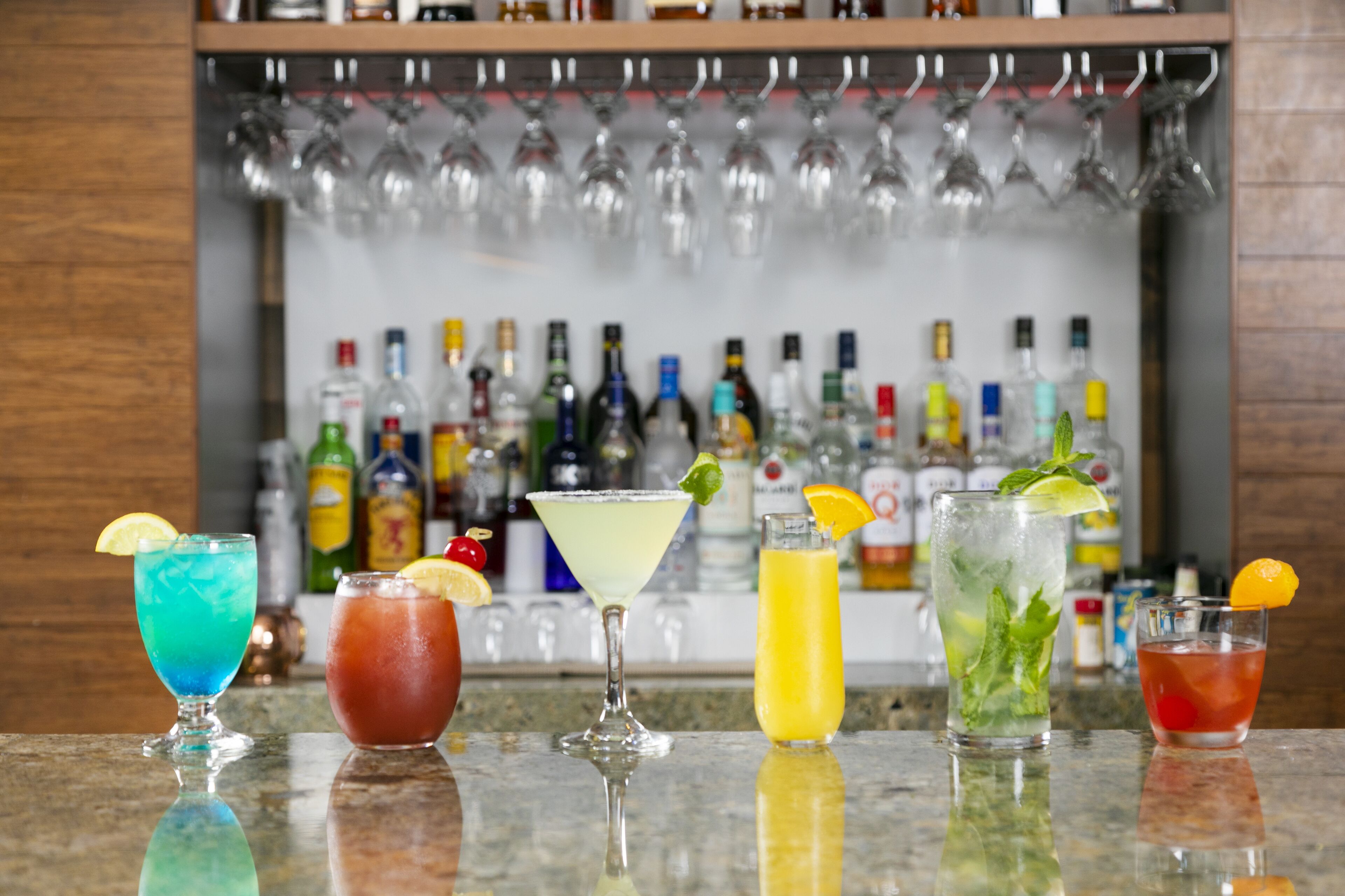 A bar with various cocktails and a selection of liquor bottles in the background.