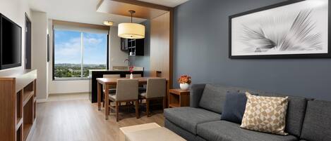 A modern living room with a grey sofa, a beige ottoman, and a dining area with a table and chairs.