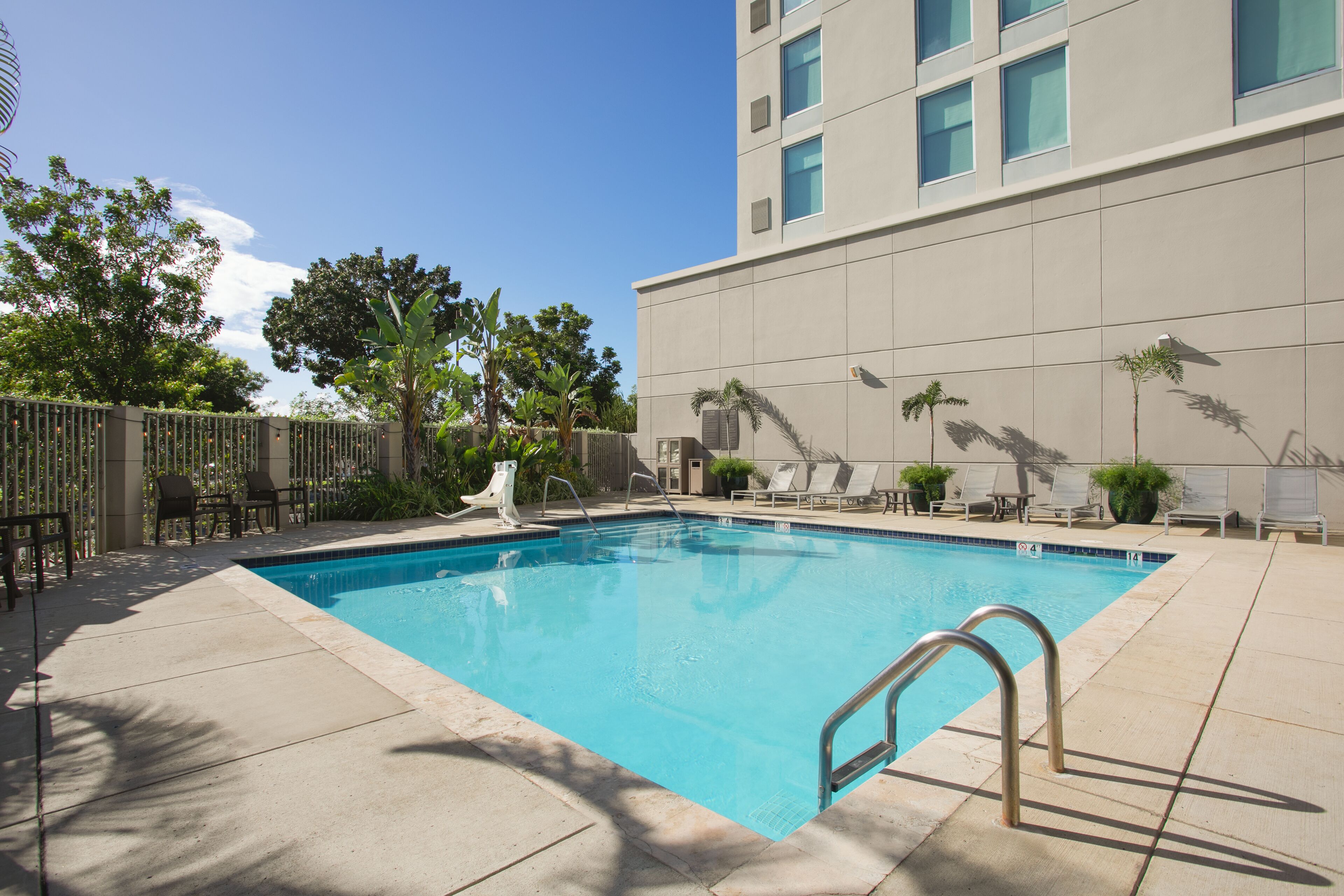 Una piscina rectangular con una escalera metálica, rodeada de un solárium con baldosas.