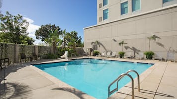 Una piscina rectangular con una escalera metálica, rodeada de un solárium con baldosas.