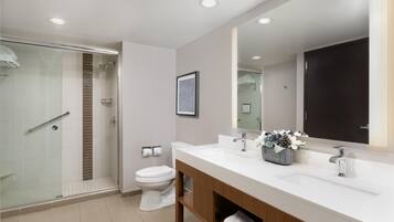 Un baño moderno con cabina de ducha de vidrio, inodoro blanco y tocador con lavabo y espejo.
