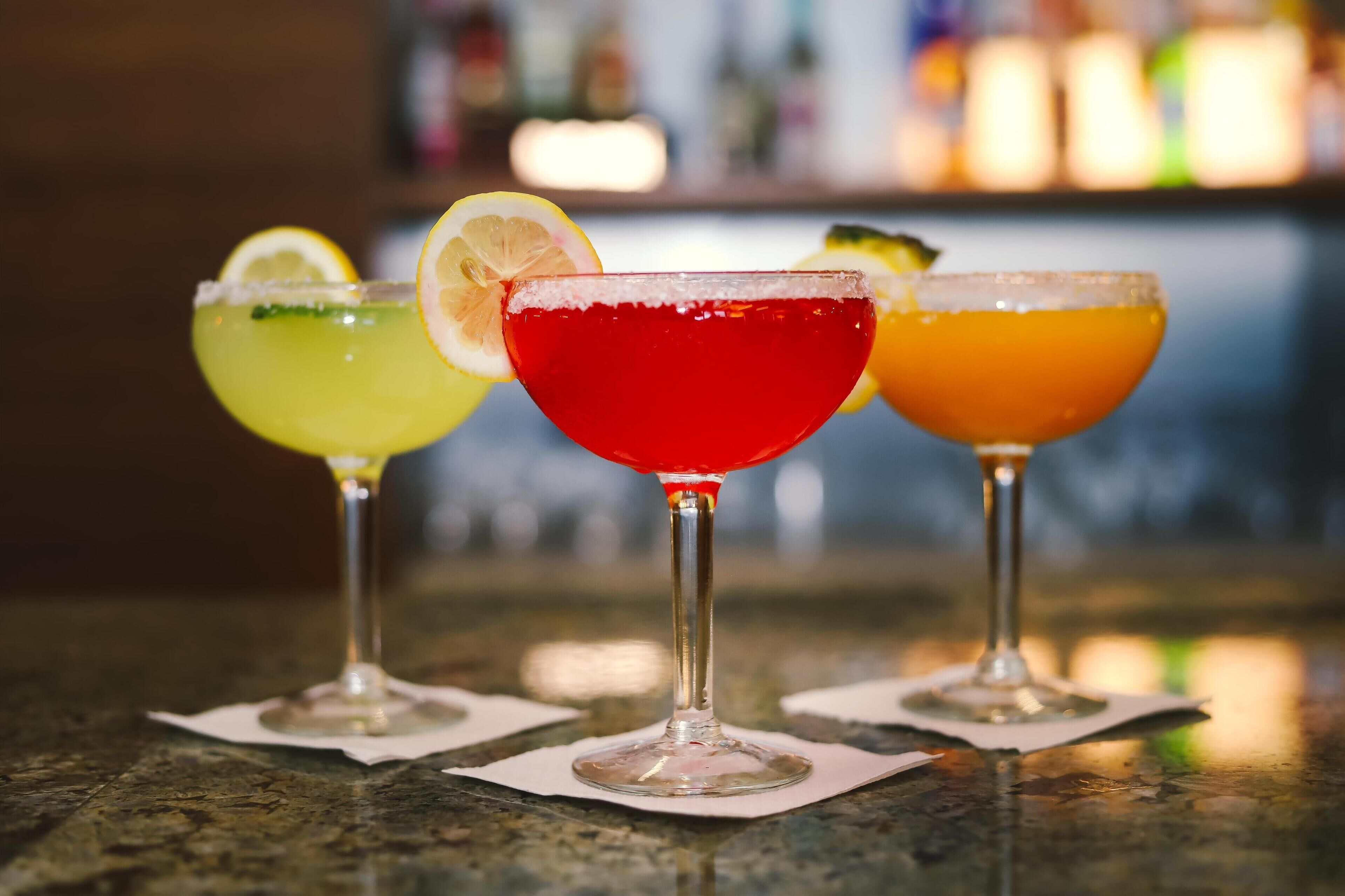 Three cocktails on a bar counter with a blurred background.