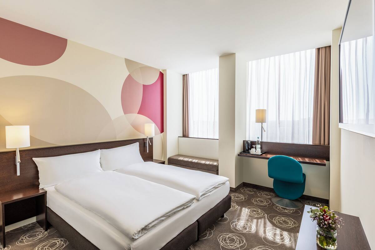 Une chambre d’hôtel avec un lit double, un bureau, une chaise et une fenêtre avec des rideaux.