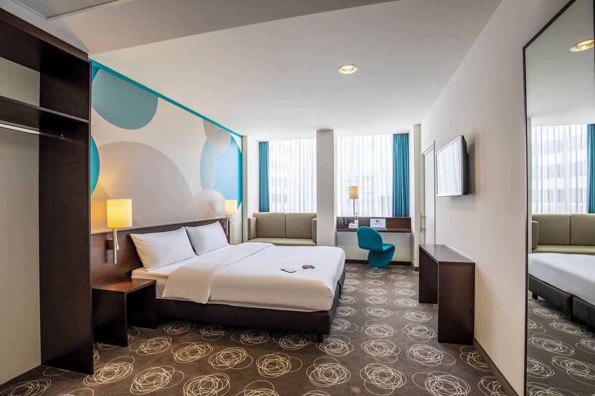 Une chambre d’hôtel comprenant un lit, une table de chevet, une lampe, un coin salon et un téléviseur.