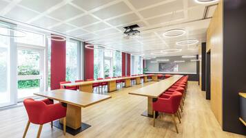 A conference room with long tables and red chairs, large windows, and a modern ceiling design.