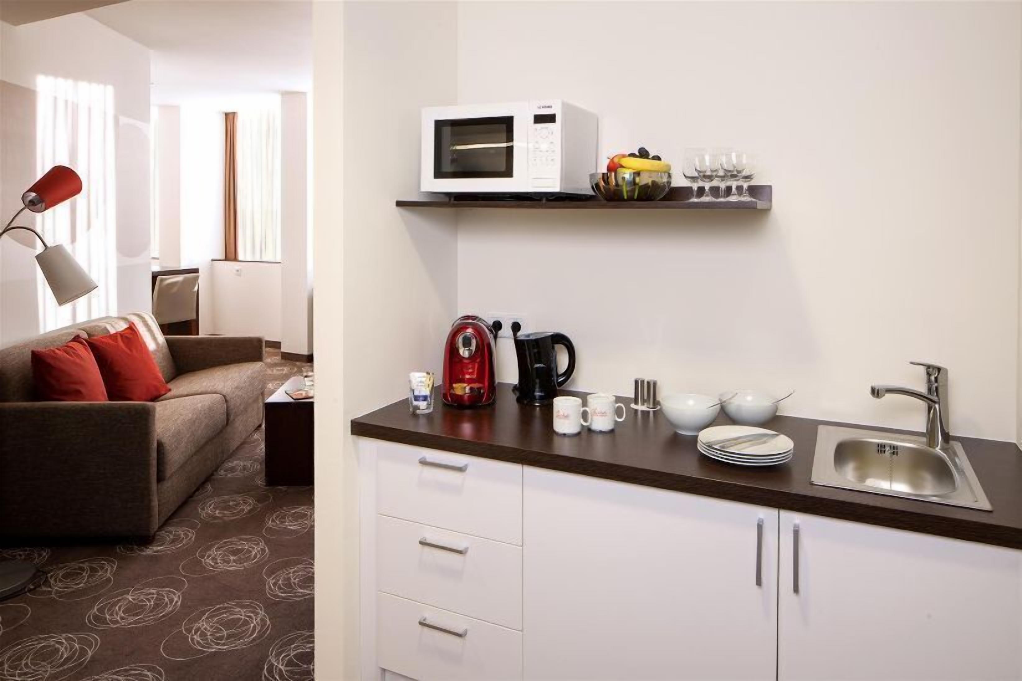 Una habitación de hotel compacta con kitchenette, un sofá, cafetera, microondas y lavamanos.