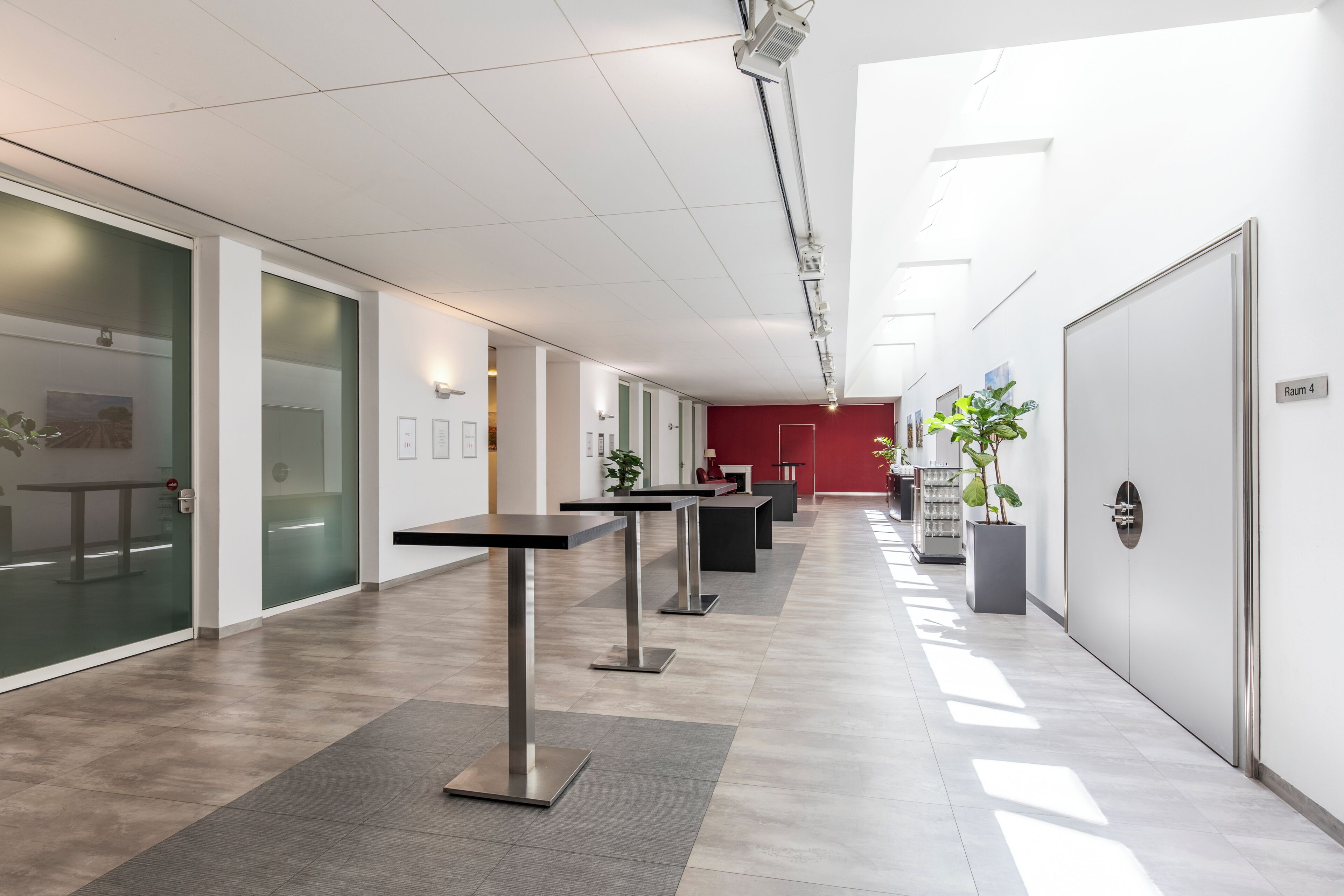 A modern office space with glass walls, metal tables, and a red accent wall.