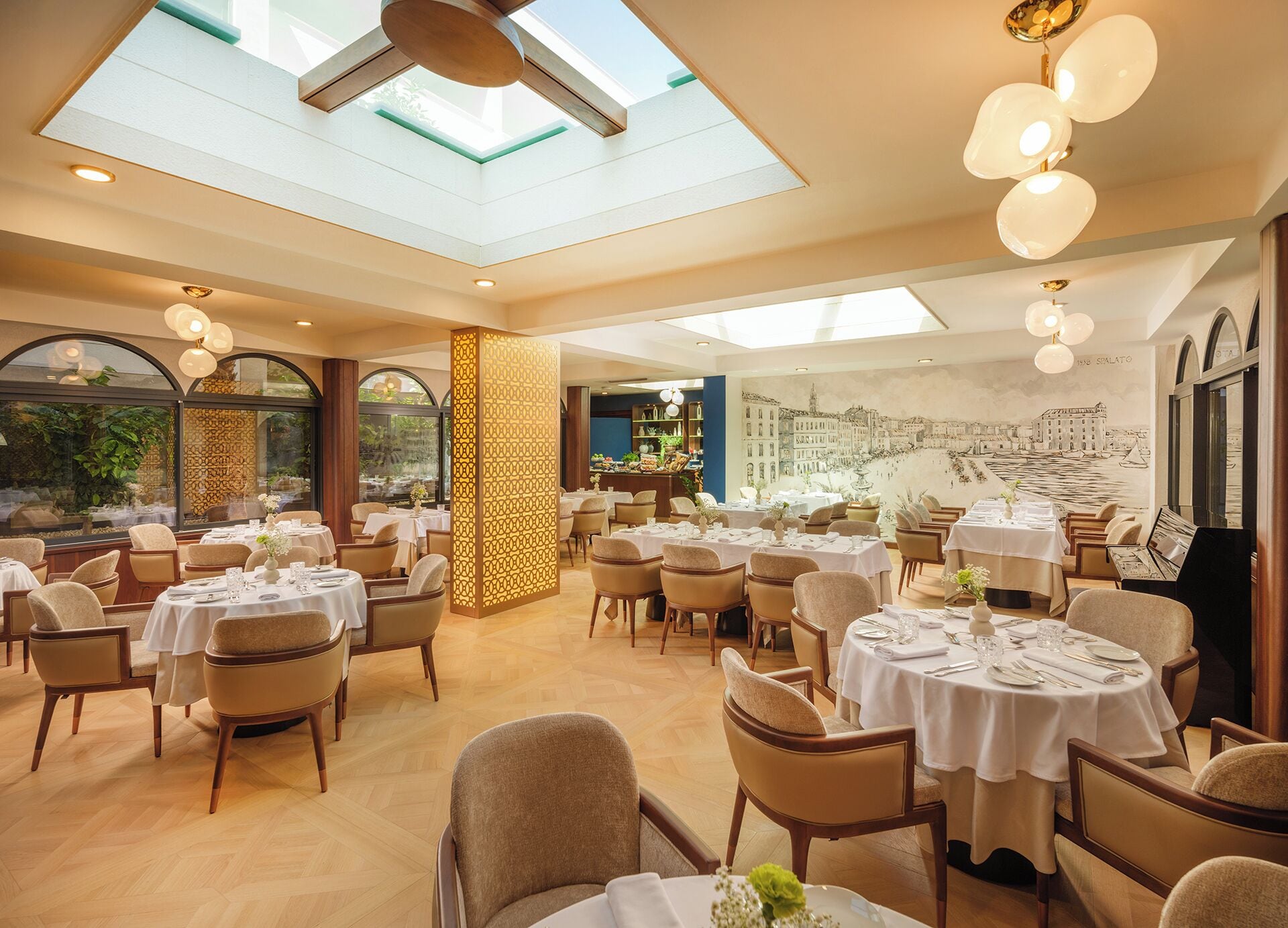 Un restaurant doté de plusieurs tables rondes, d’un plafond haut orné de verrières et d’une fresque représentant un paysage urbain.