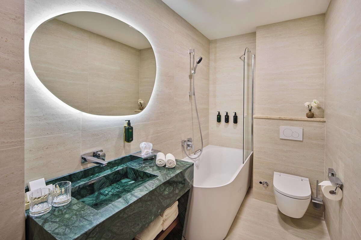 A modern bathroom with a freestanding bathtub, a large mirror, and a marble sink.