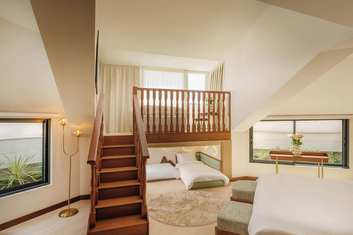 A bedroom with a wooden staircase, a bed, a desk, and a window with a view.
