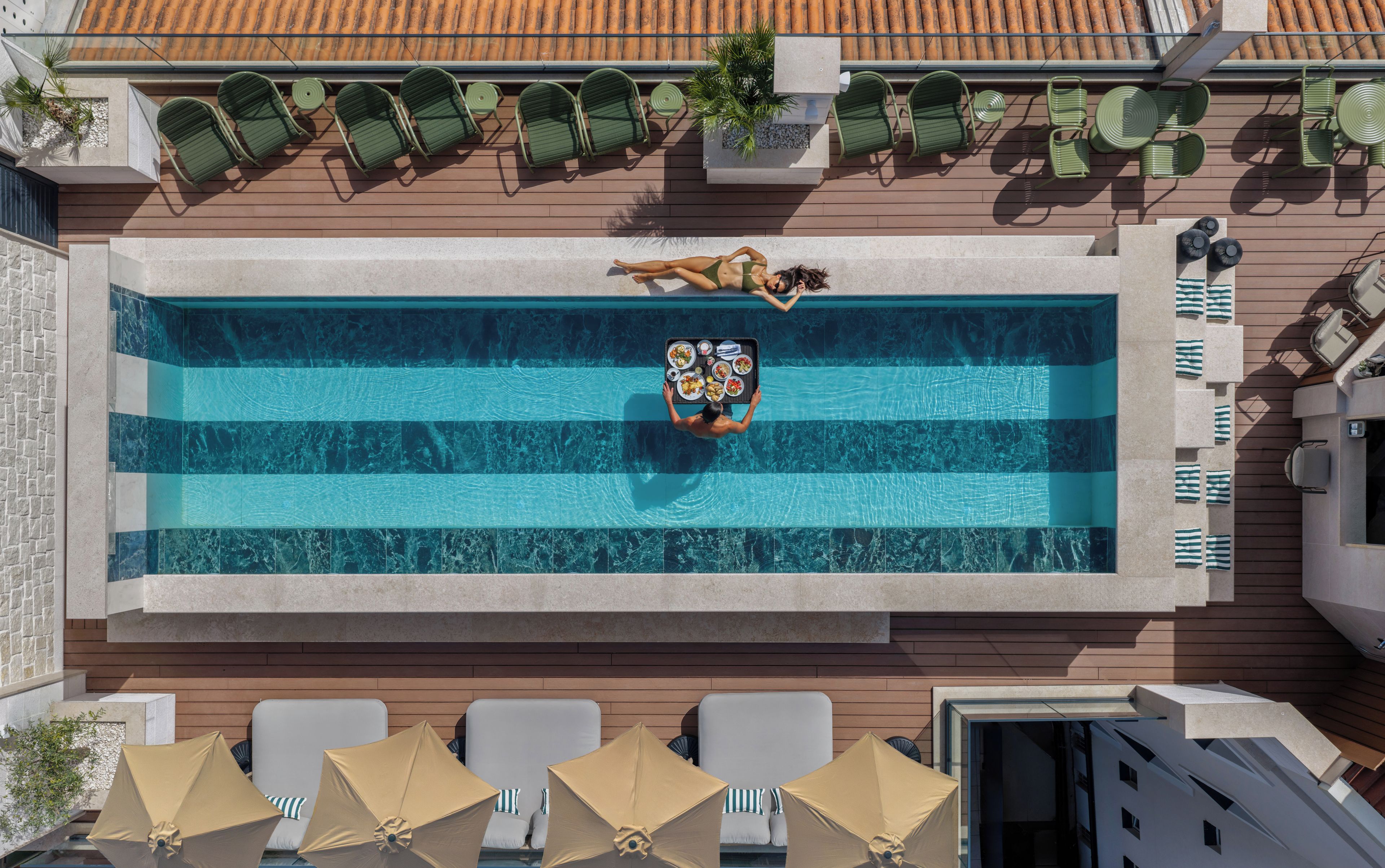 An outdoor swimming pool with lounge chairs and umbrellas, surrounded by a wooden deck and a tiled roof.