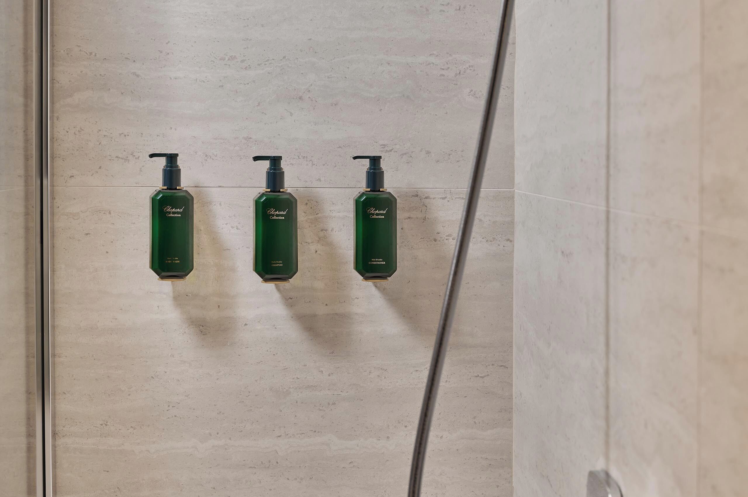 Three green bottles of lotion on a tiled wall.