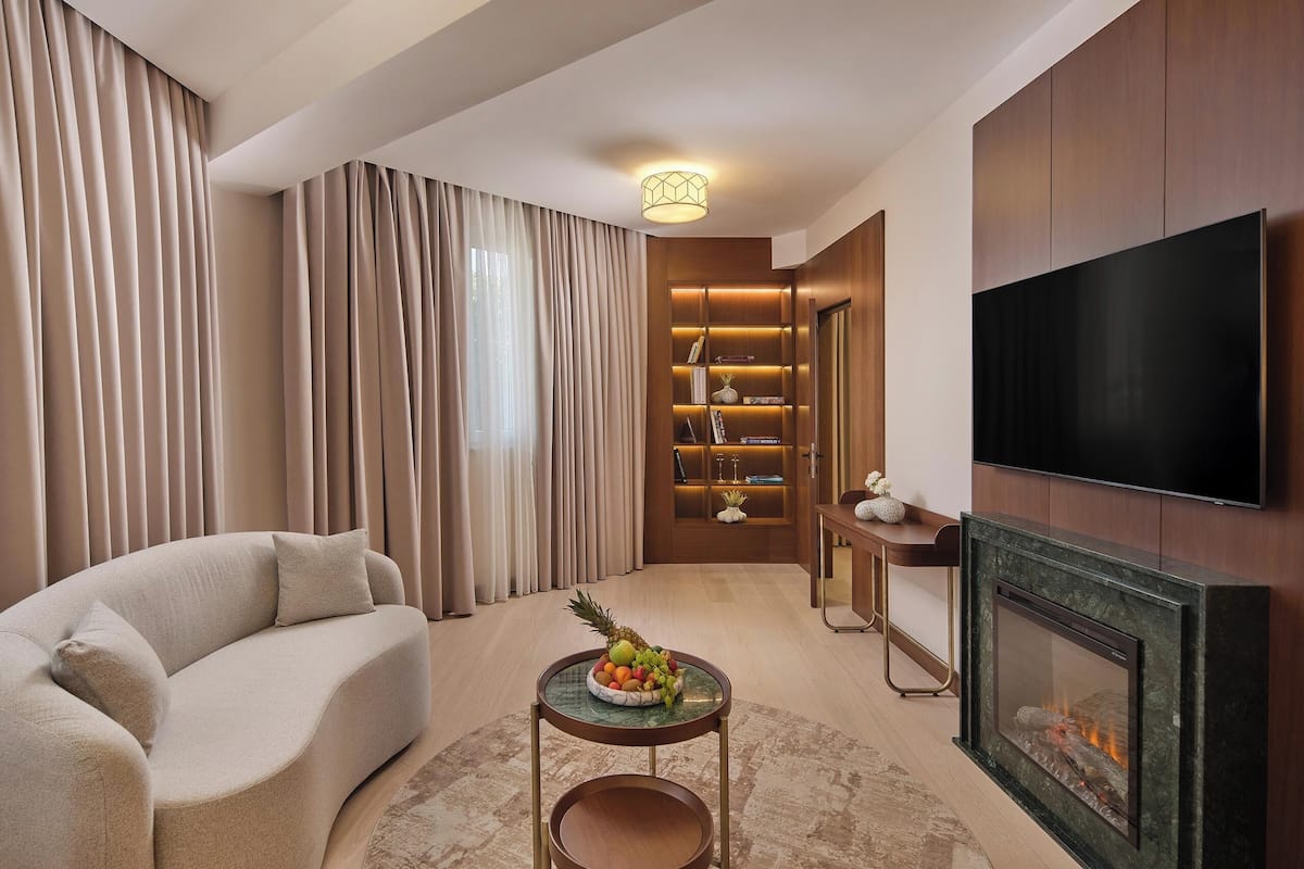 A modern living room with a sofa, a small round table with fruit, a fireplace, a TV, and a bookshelf.