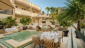 A poolside area with tables and chairs, a pool, and surrounding greenery. - Palazzo President (Split)