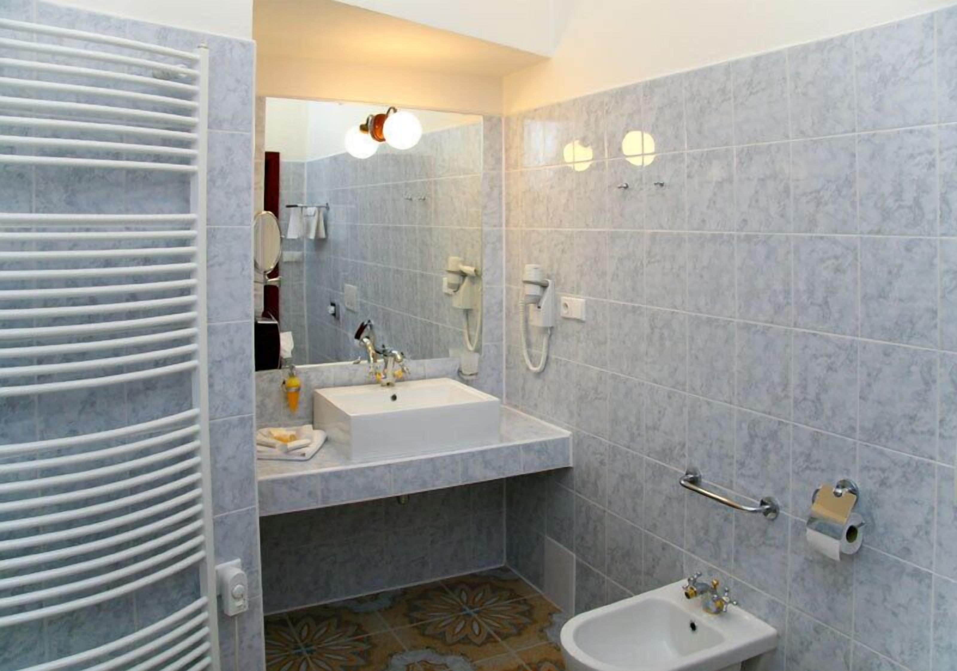 A bathroom with a sink, mirror, towel rack, and a shower area.