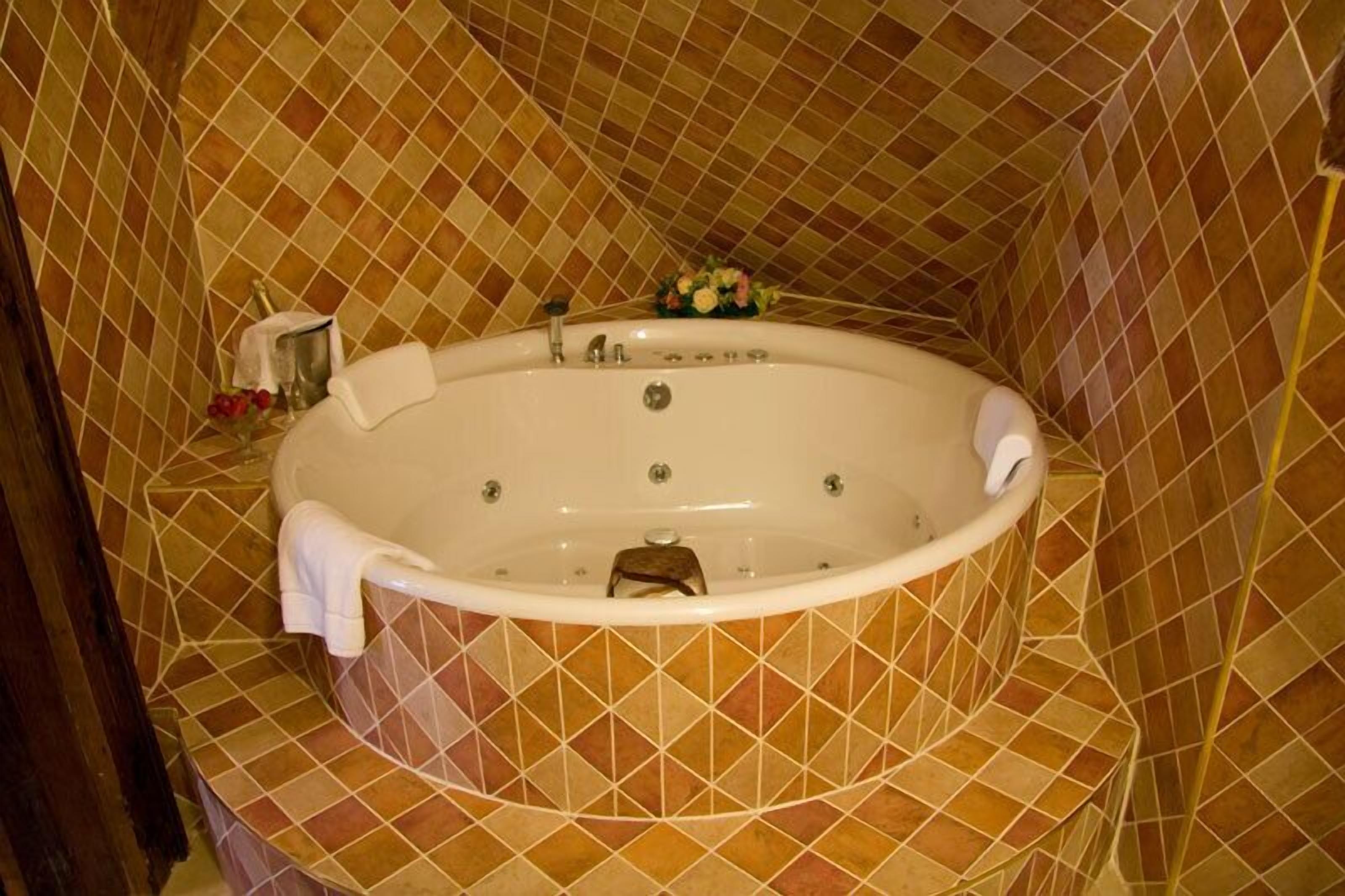 A large, freestanding bathtub with a white interior, surrounded by a patterned tile floor and walls.