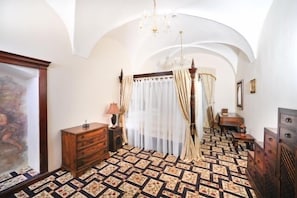 A bedroom with a patterned floor, a wooden dresser, a bed with curtains, and a chandelier.