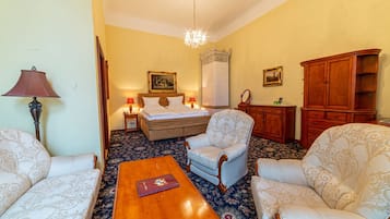Una habitación con una cama, dos sillones, una mesa de centro de madera, una lámpara y una araña.