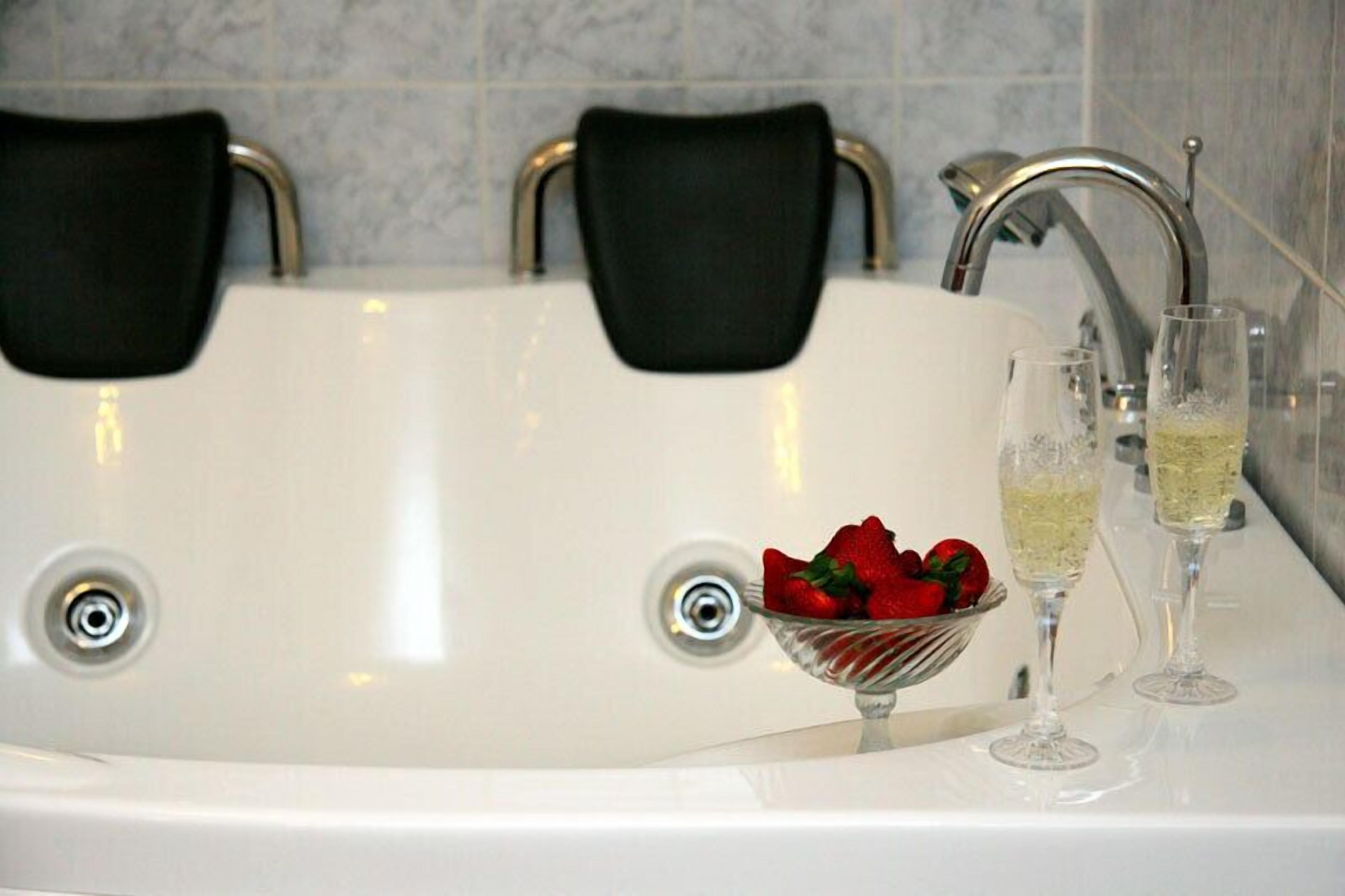Une baignoire avec deux chaises noires, un saladier de fraises et deux coupes de champagne.