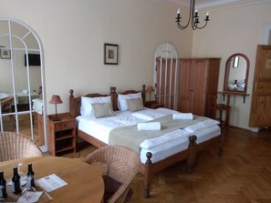 A neatly arranged bedroom with a large bed, wooden furniture, a dining table with bottles, and a mirror.