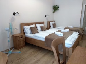 Habitación de hotel con dos camas, cabeceros de madera, sábanas blancas, almohadas marrones y una mesita de noche con lámpara.