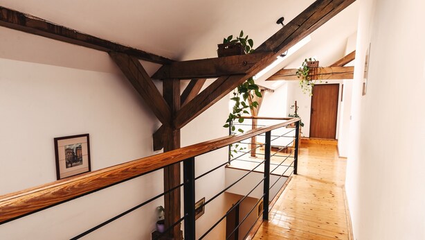 Una escalera de madera con barandilla de metal, paredes blancas y piso de madera.