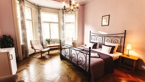 Un dormitorio con cama, una silla, una mesita de noche, una lámpara y una ventana con cortinas.