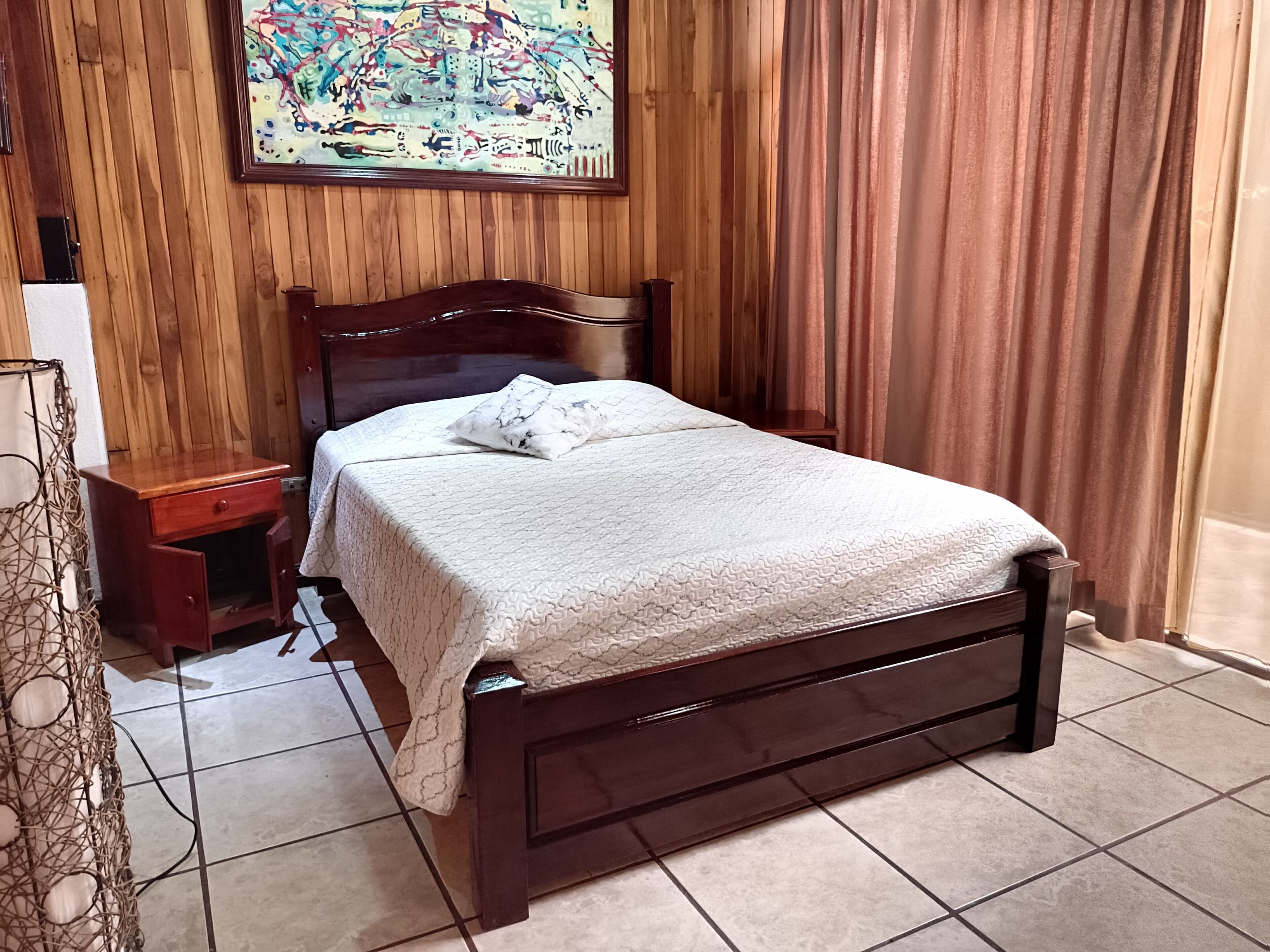 Un lit bien fait, avec une couette blanche, une tête de lit en bois, une petite table de chevet et un tableau accroché au mur.