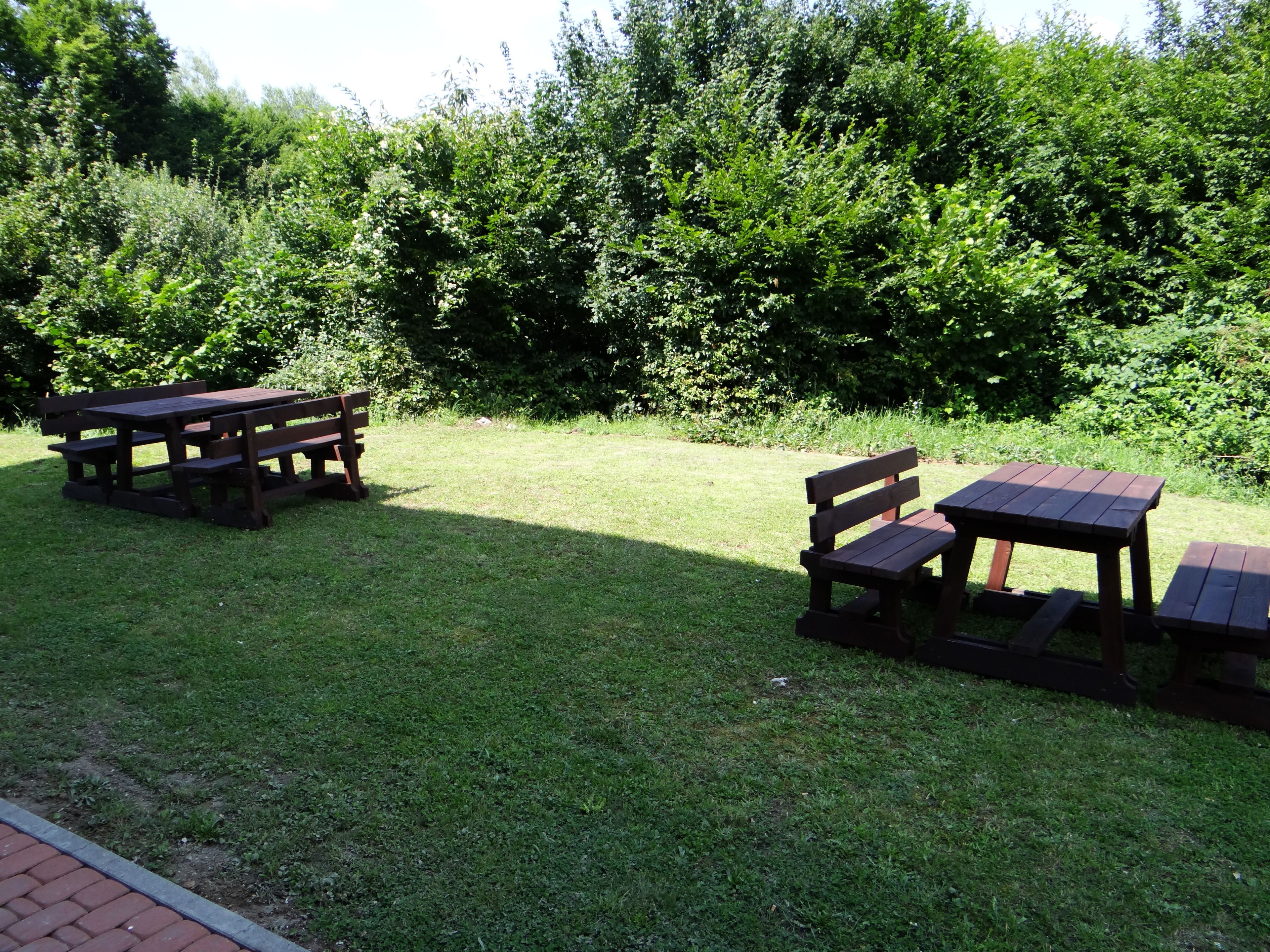 A picnic area with wooden benches and tables, surrounded by lush greenery.