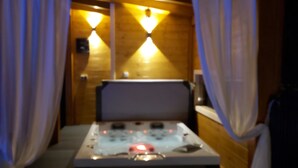 Een kamer met weinig licht, een bed, gordijnen en een wandlamp.