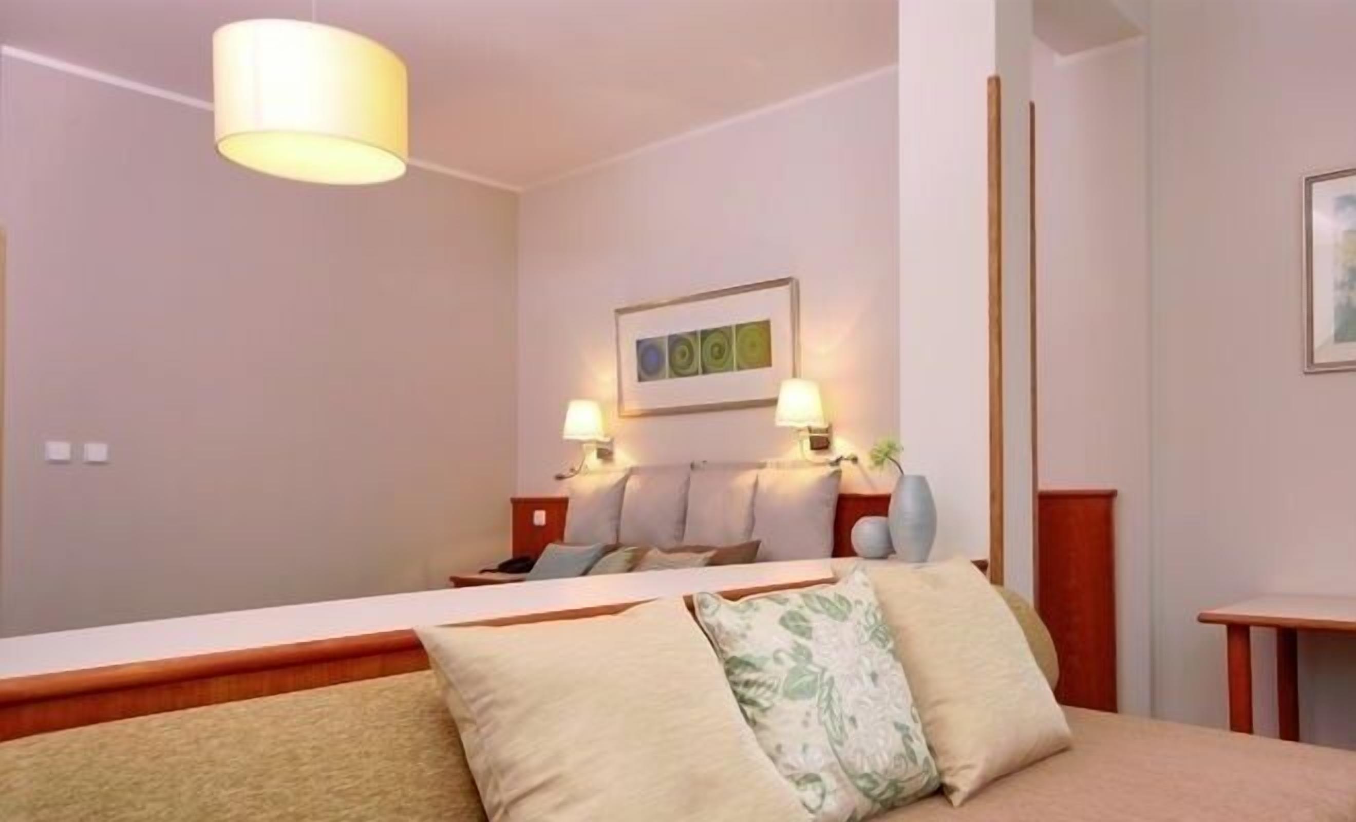 A hotel room with a bed, two bedside lamps, a wall-mounted artwork, and a small table with a vase.