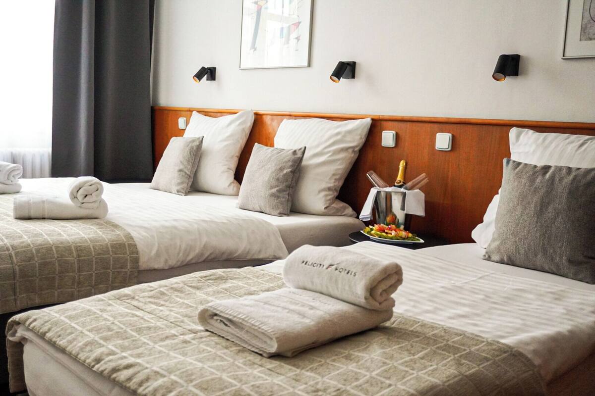A hotel room with two beds, each with a neatly folded towel and a bottle of champagne.