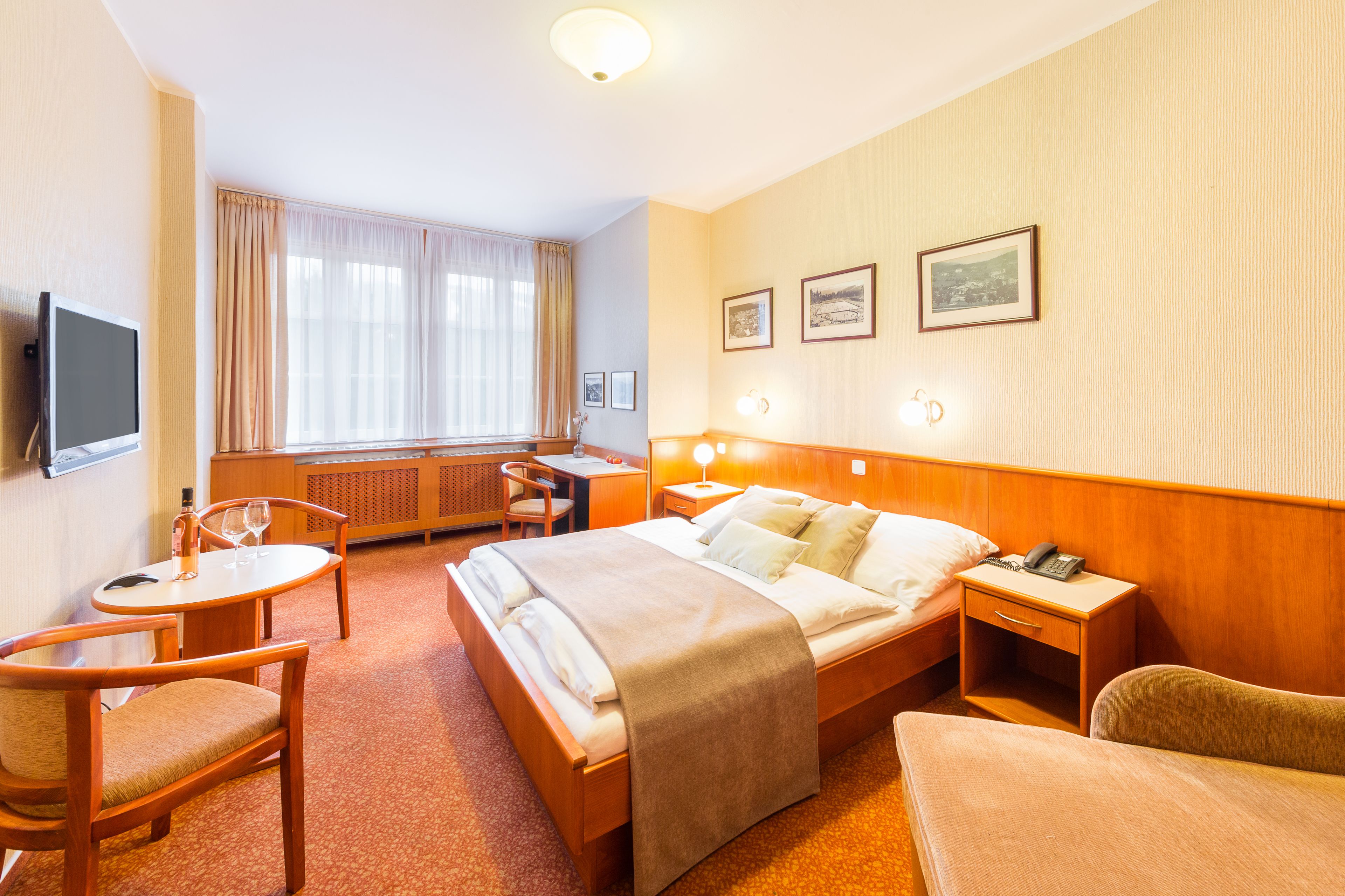A hotel room with a bed, a desk, a chair, a television, and a window with curtains.