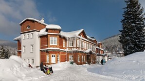 Un grande edificio di legno con numerose finestre e un tetto imbiancato dalla neve, circondato da neve e alberi.