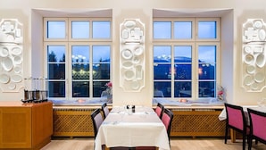 Zona pranzo con vista sulla città attraverso ampie finestre, una panca in legno e un tavolo apparecchiato per due.