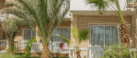 Un hôtel à plusieurs étages doté de balcons, de palmiers et d’une pelouse bien entretenue.