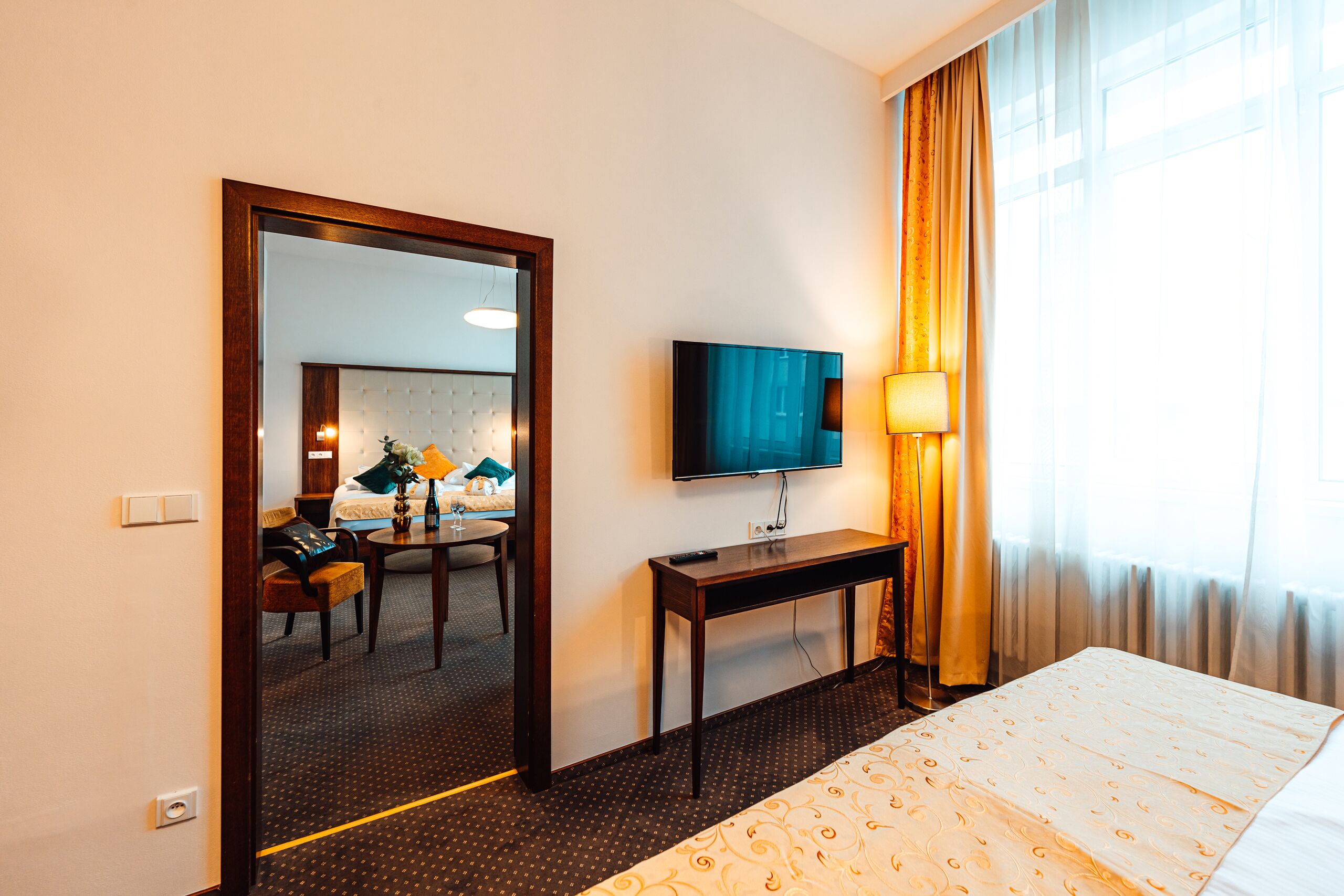 Camera d'albergo con un letto, una TV a parete, una scrivania con una lampada e un grande specchio.