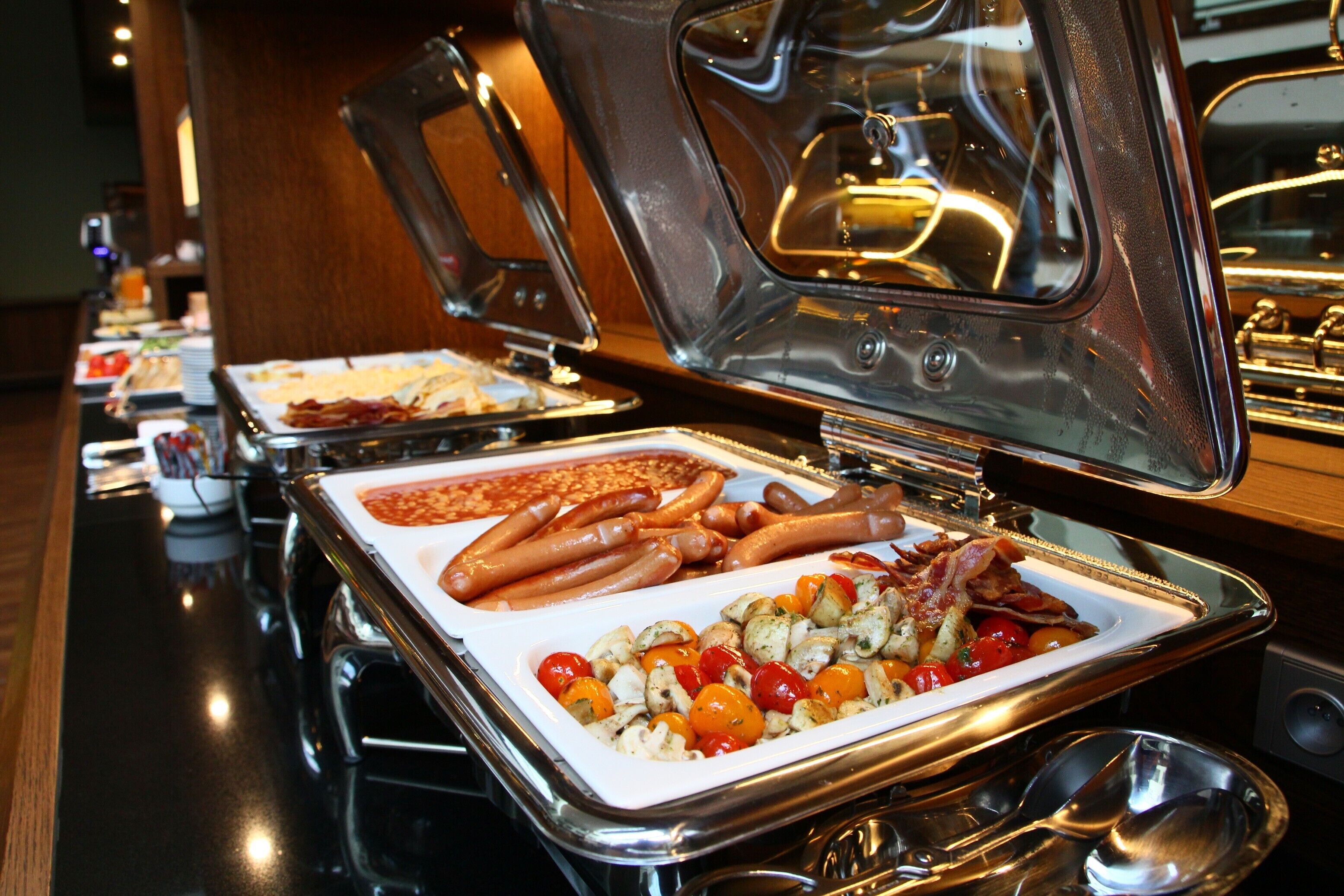 Ein Buffet mit verschiedenen Speisen, darunter Würstchen, Speck und geröstetem Gemüse.