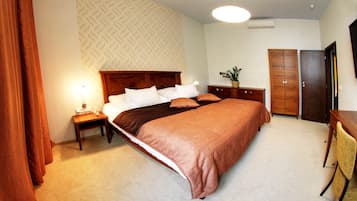 A neatly arranged bedroom with a large bed, a bedside table with a lamp, a wardrobe, and a desk with a chair.