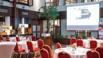 Un salón de conferencias con varias mesas, sillas rojas y una pantalla de proyector mostrando una presentación.