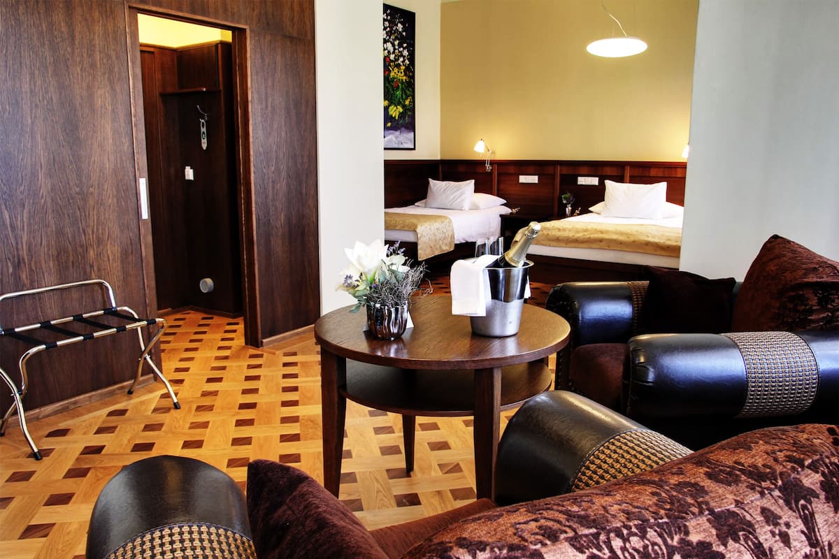 A hotel room with a wooden floor, a dining table with a vase of flowers, a sofa, and a bed with white linens.