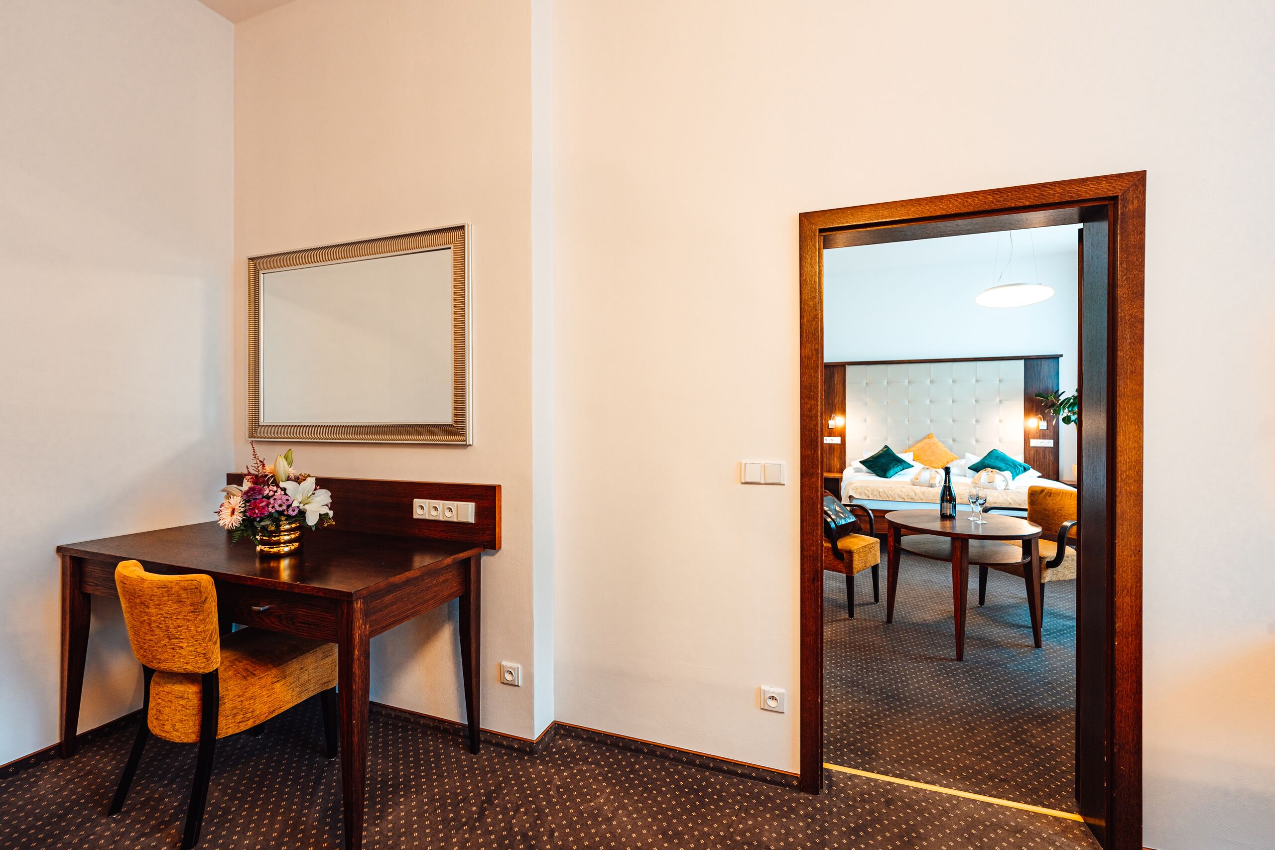 A hotel room with a wooden desk, a chair, a mirror, and a bed with a tufted headboard.