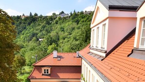 A building with a red-tiled roof, a courtyard with outdoor seating, and a lush green hillside in the background. - Castle Residence Praha (Prague)
