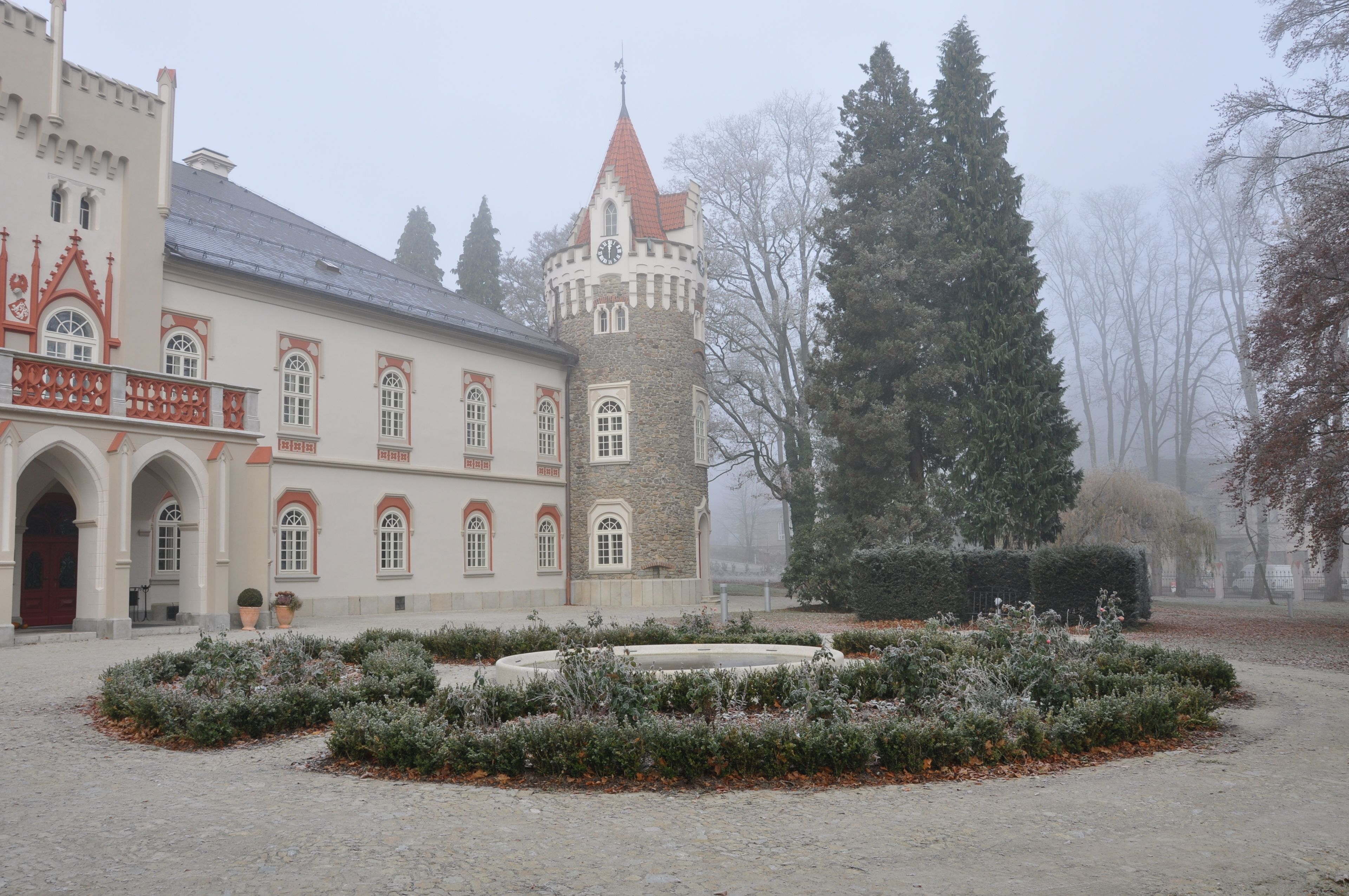 A historic building with a tower, arched windows, and a courtyard with a circular garden.