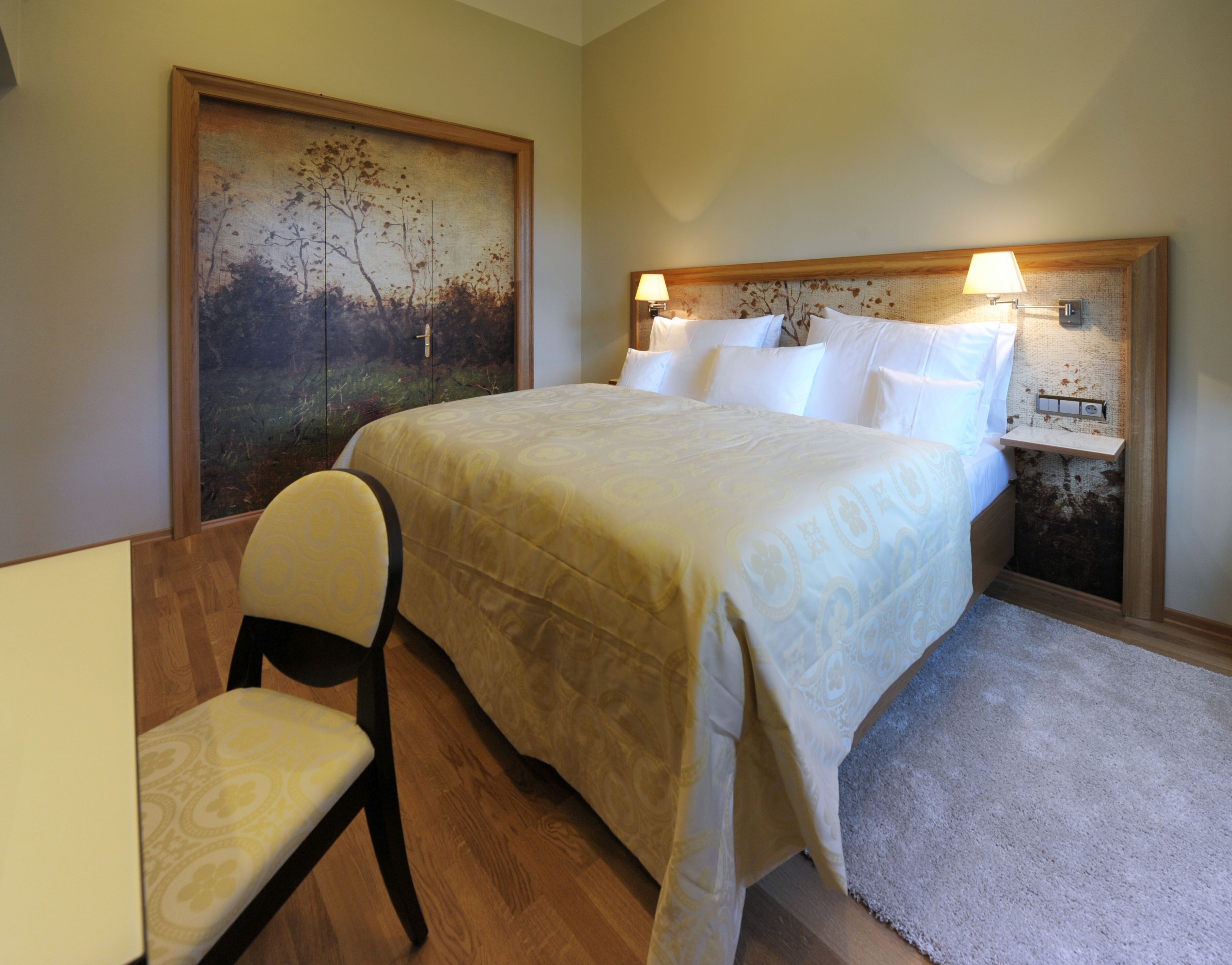 A bedroom with a bed, a chair, a nightstand, and a painting on the wall.