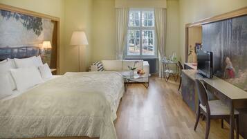 Een hotelkamer met een groot bed, een bureau met een computer, een stoel, een klein tafeltje met een bloemenvaas en een raam met gordijnen.