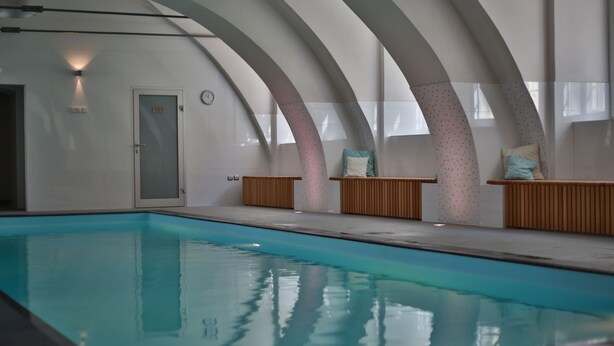Una piscina interior de diseño moderno, con techos abovedados y zonas de estar de madera.